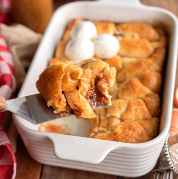 Crescent Roll Apple Dumpling on a spatula in front of pan of them.