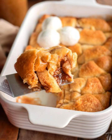 Crescent Roll Apple Dumpling on a spatula in front of pan of them.
