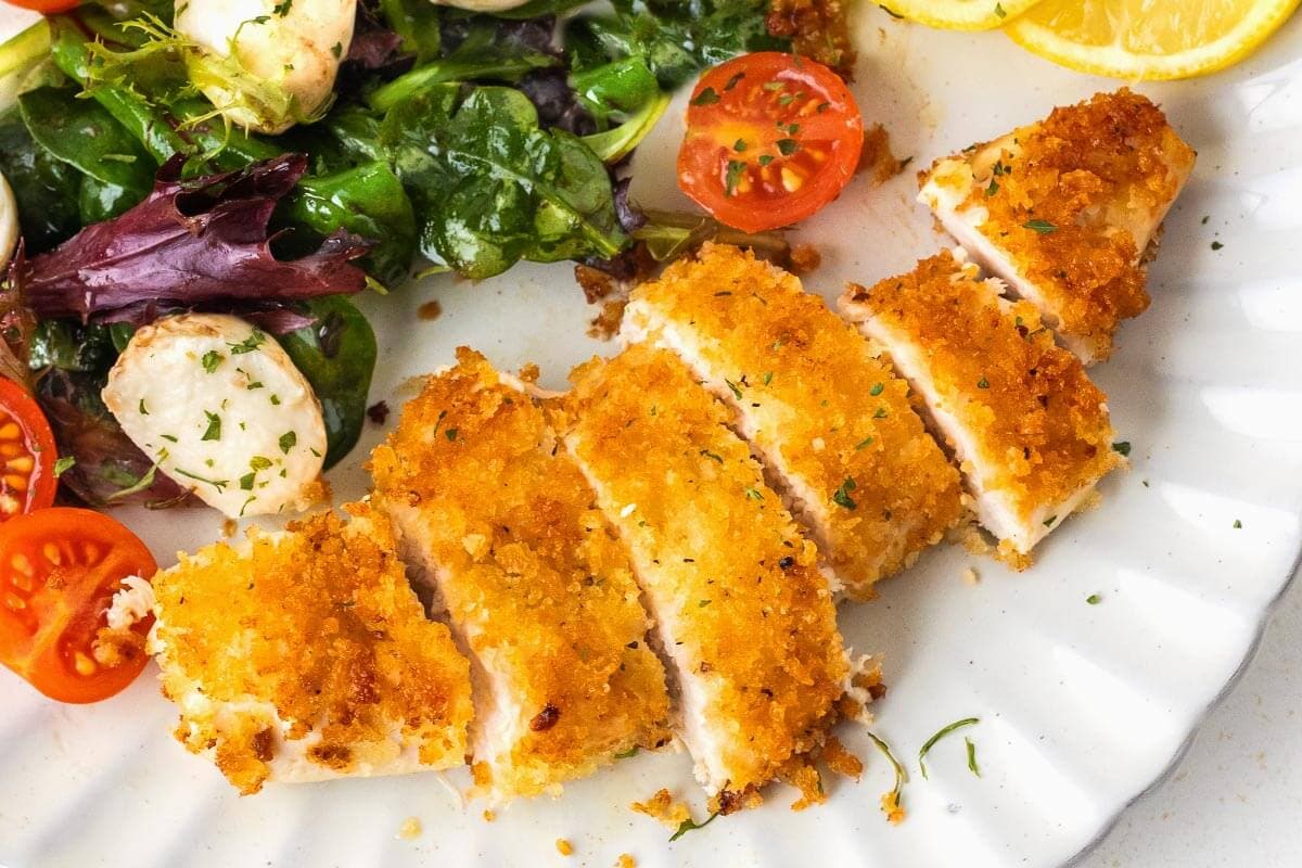Crispy Pan-Fried Chicken Cutlets on a white plate with salad