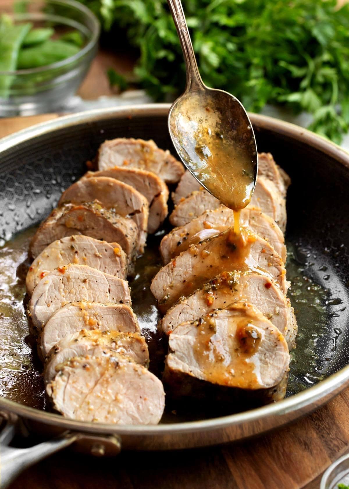 2 Pork Tenderloins sliced in a skillet with spoon drizzling sauce on them.