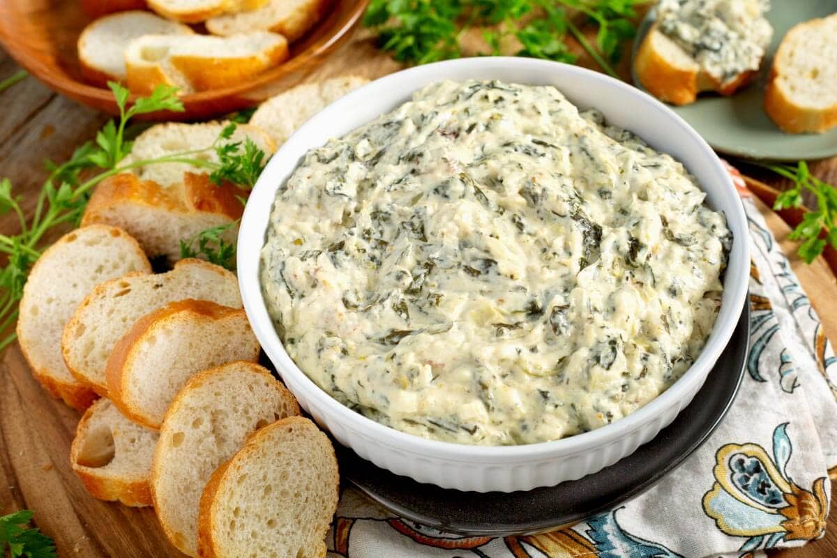 Slow Cooker Spinach Artichoke Dip in grey bowl with bread slices.