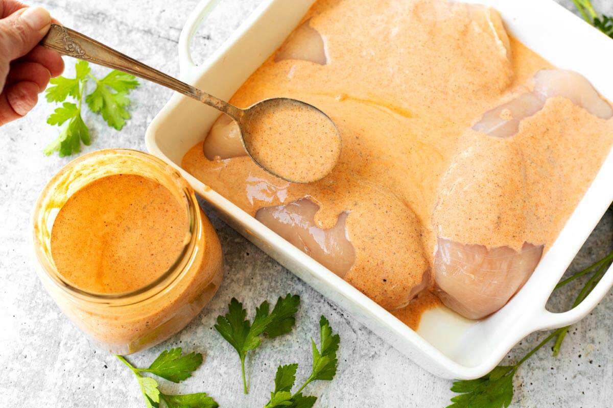 Southwest Buttermilk Chicken Marinade in a mason jar with a spoonful pouring over chicken breasts in a white dish.