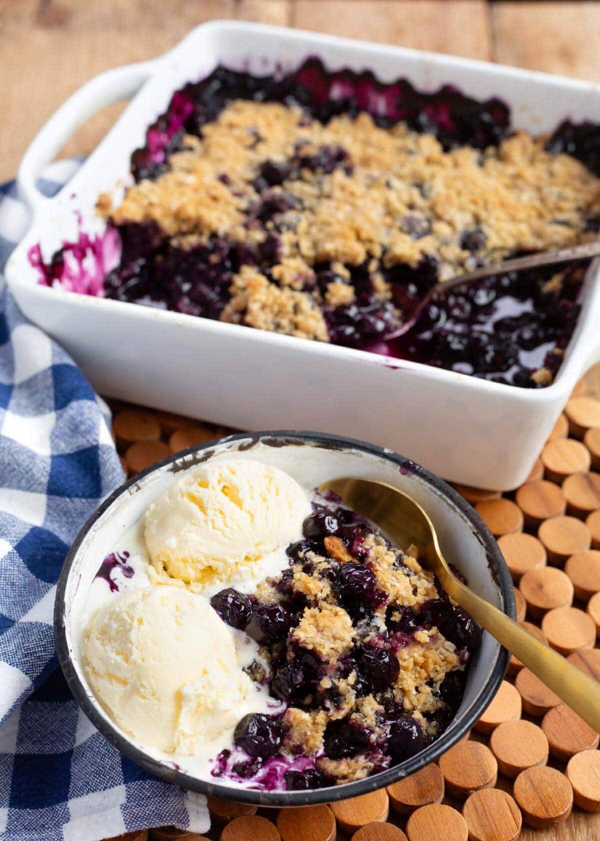 Easy Blueberry Crisp in baking dish and a bowl with ice cream and spoon