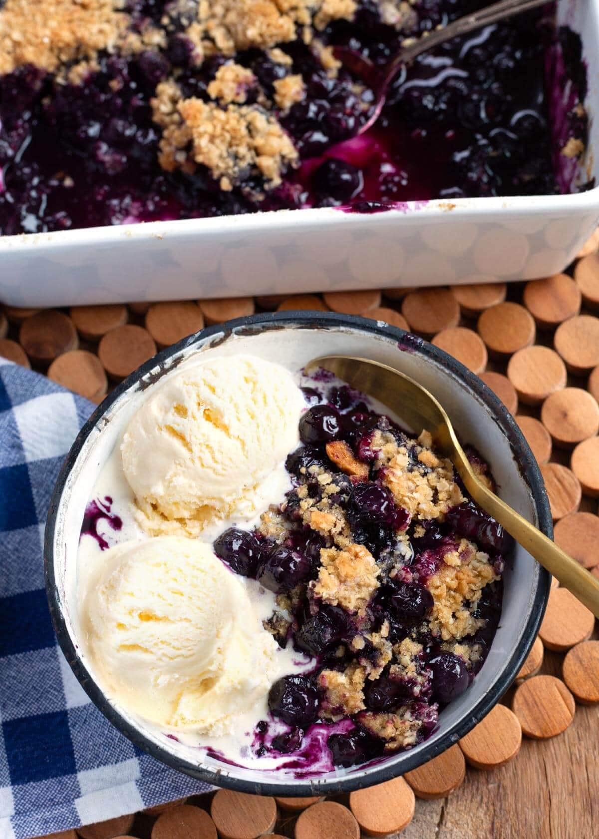 Easy Blueberry Crisp in baking dish and a bowl with ice cream and spoon