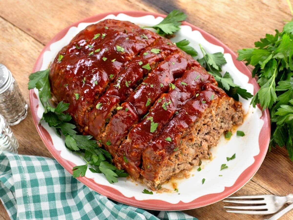 top down view of partially sliced cooked meatloaf on a white platter on wood surface