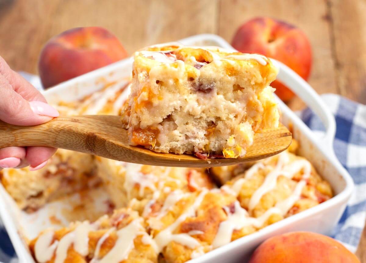 peach butter swim biscuit on a wood spatula with baking dish full underneath