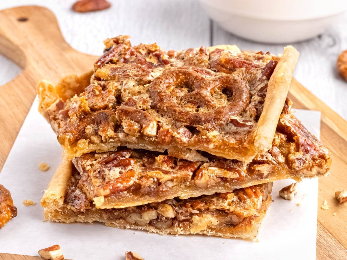 3 pieces of pecan slab pie on a wood board with parchment