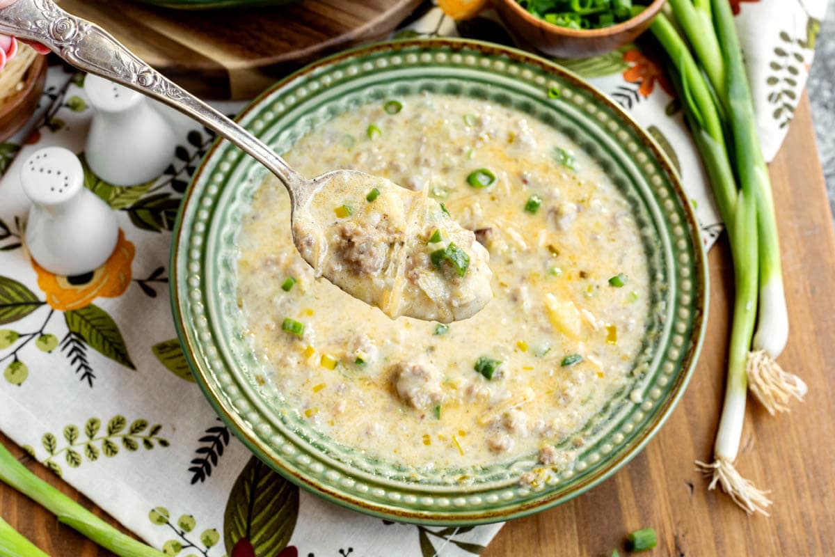 potato leek sausage soup in a green bowl with spoonful hovering above it.