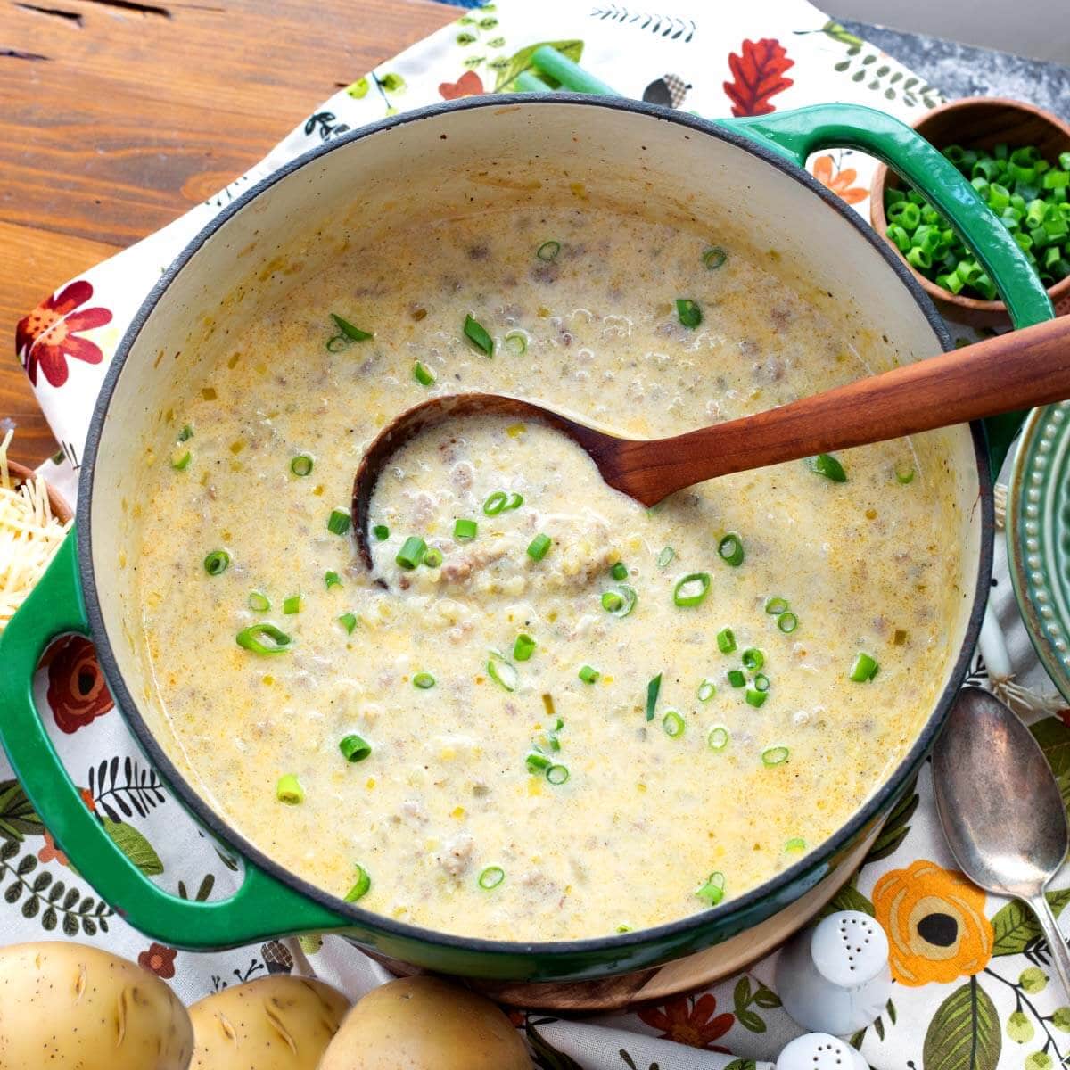 potato leek sausage soup in a green Dutch oven with a wooden ladle.