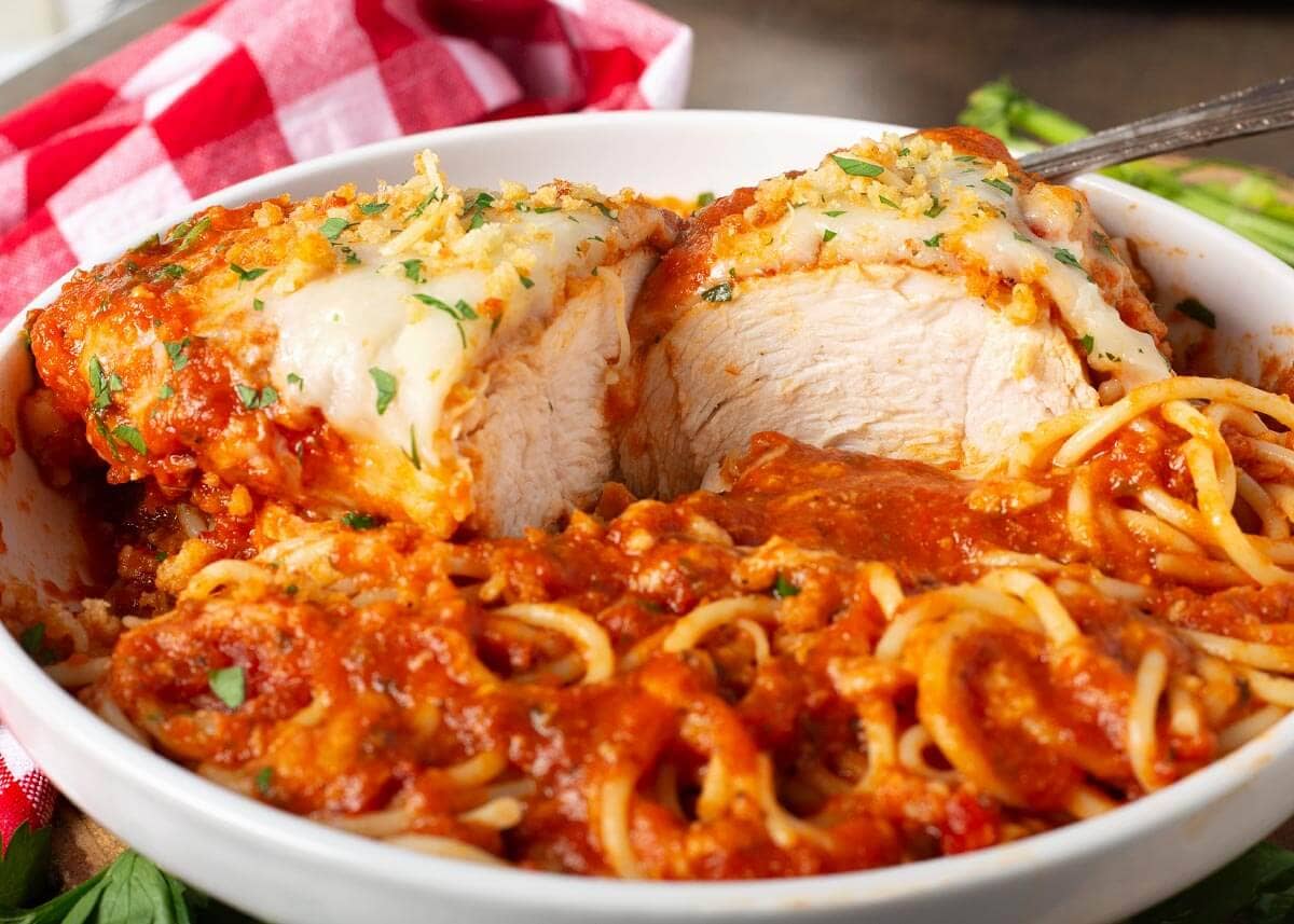 slow cooker chicken parmesan cut in half in a white bowl with spaghetti