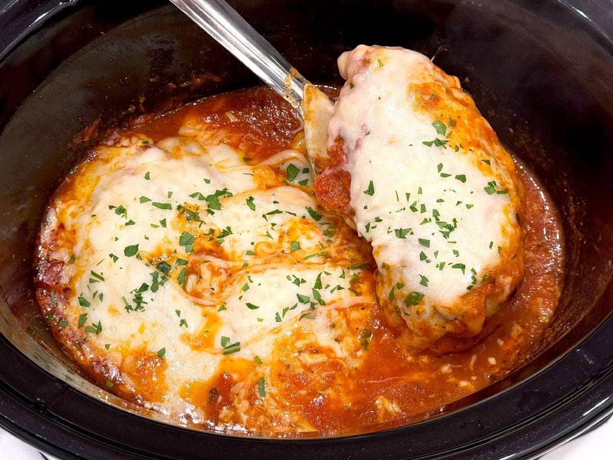 lifting a chicken parmesan breast out of the slow cooker with a spoon