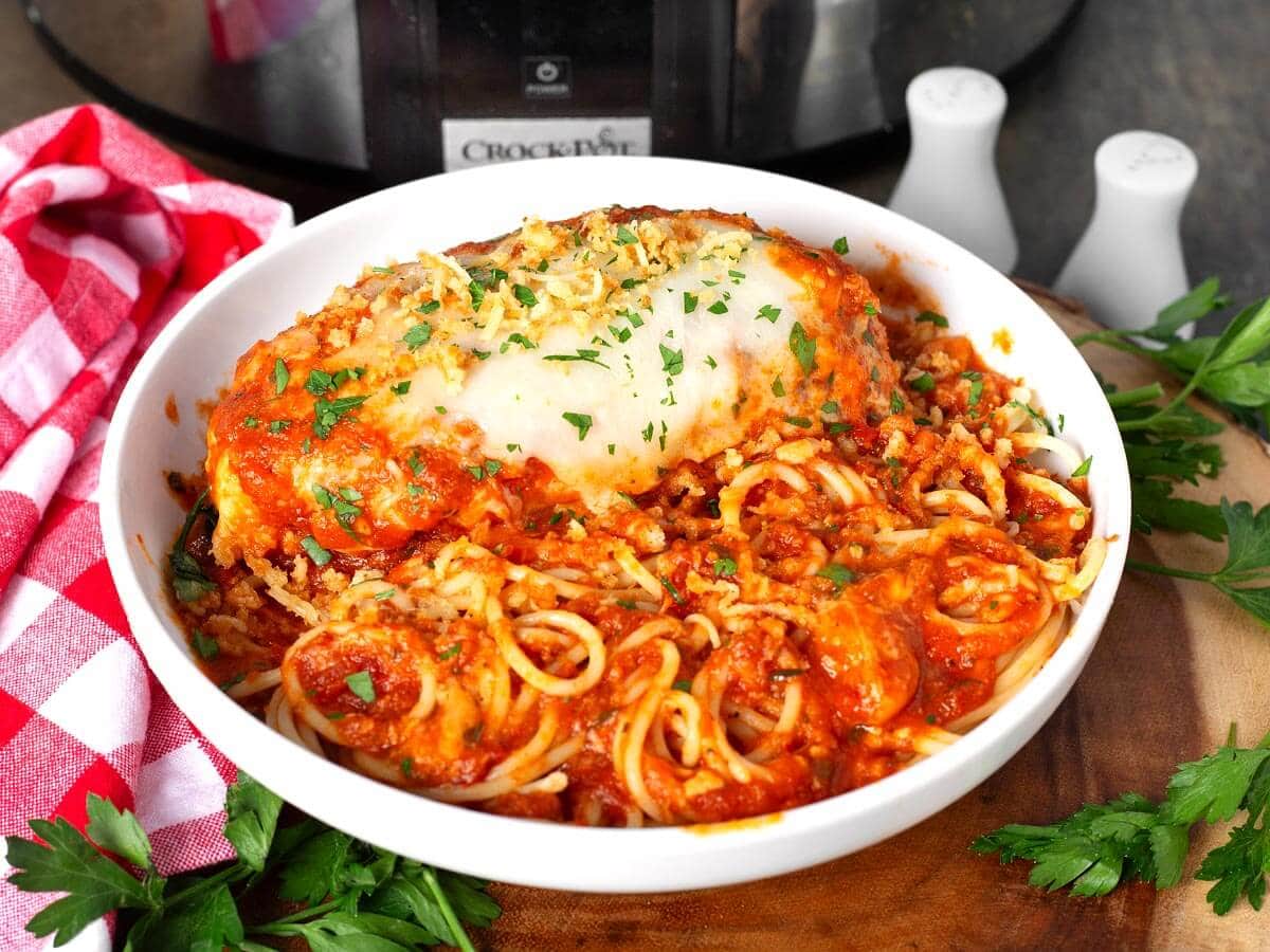 crockpot chicken parmesan in a white bowl with spaghetti