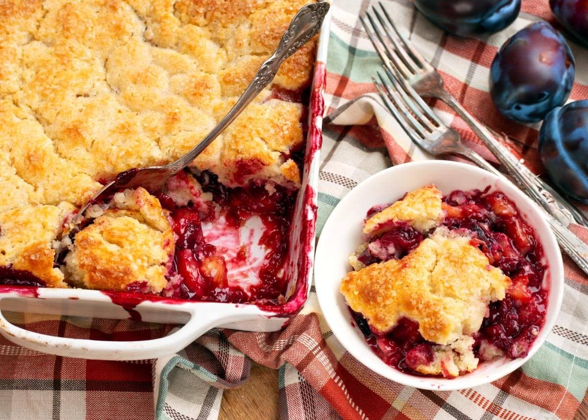 plum cobbler in a white baking dish and a white bowl with a serving in it