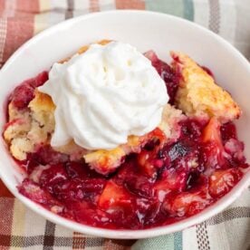 serving of plum cobbler in a white dish with whipped topping on top