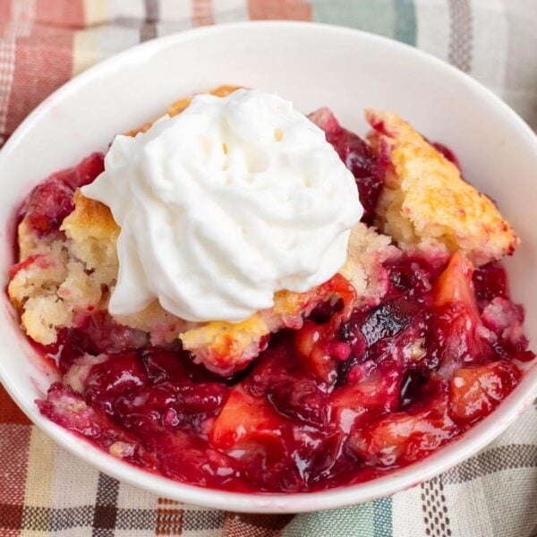 serving of plum cobbler in a white dish with whipped topping on top