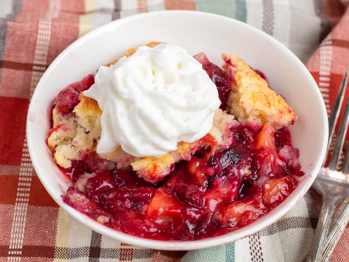 serving of plum cobbler in a white dish with whipped topping on top