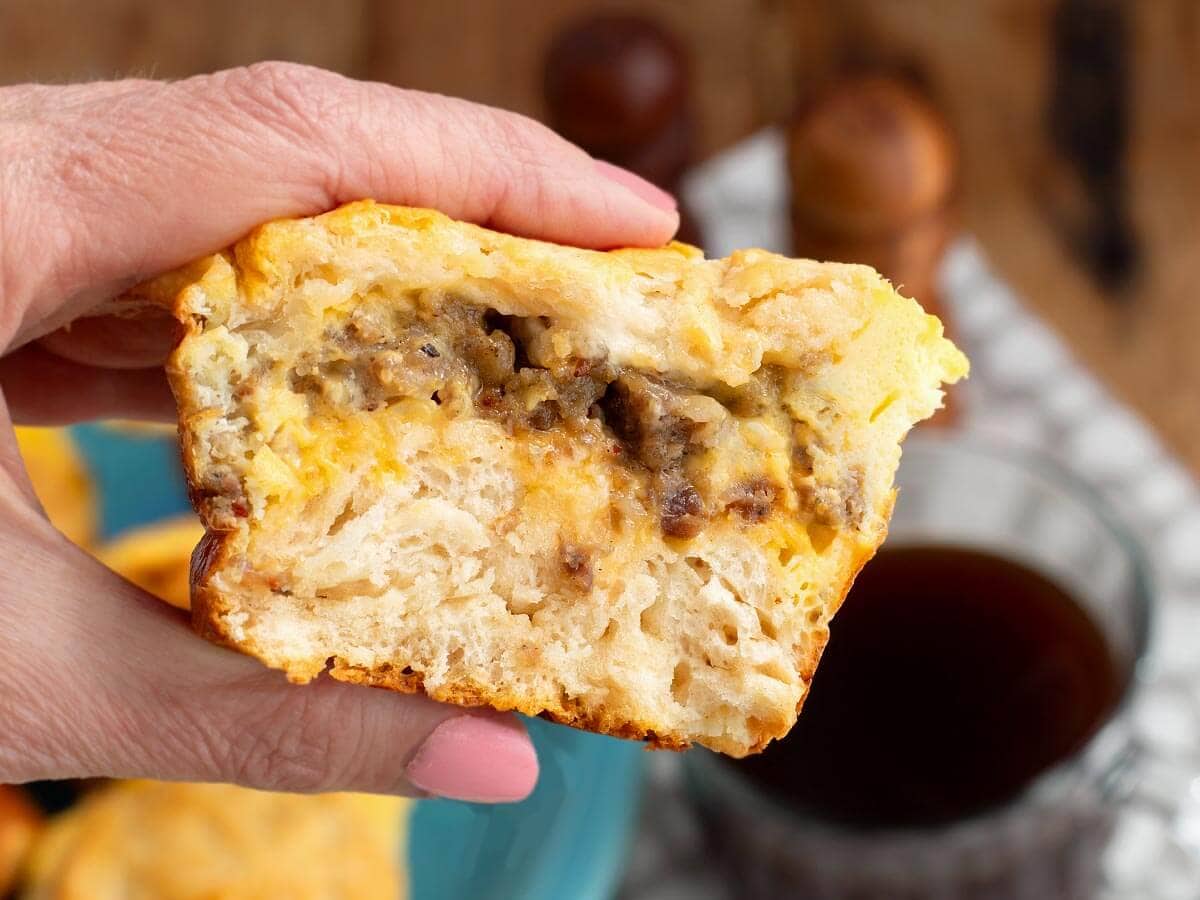 hand holding a sliced open egg muffin with sausage and cheese