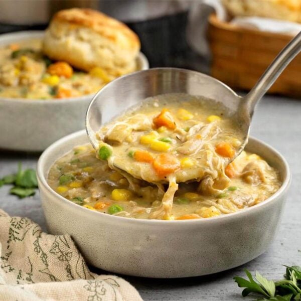 Ladle lifting creamy Instant Pot Chicken Pot Pie filling with shredded chicken, carrots, peas, and corn from a bowl