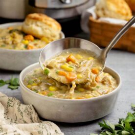 Ladle lifting creamy Instant Pot Chicken Pot Pie filling with shredded chicken, carrots, peas, and corn from a bowl