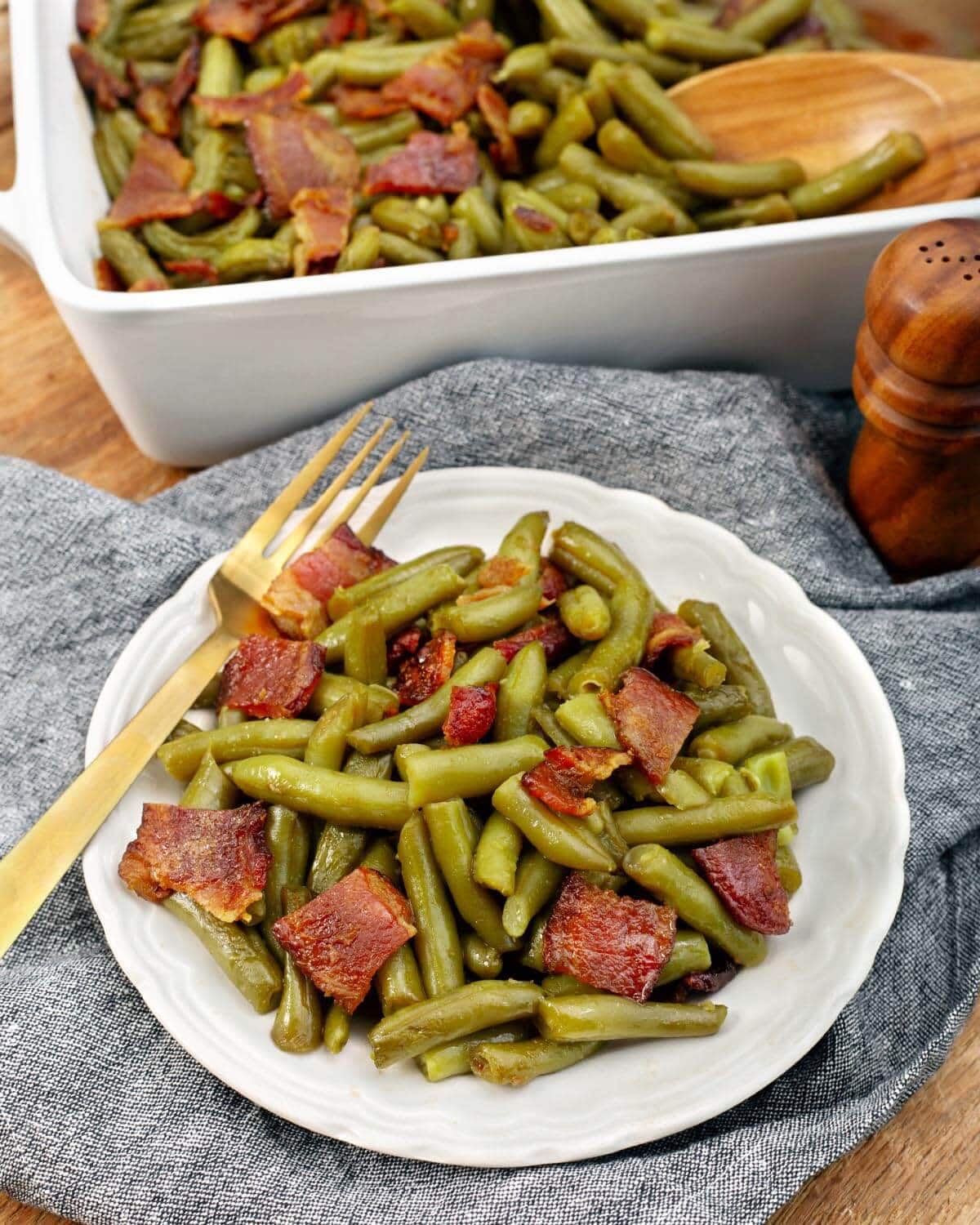 Plate of green beans and browned bacon pieces with the baking dish in the background