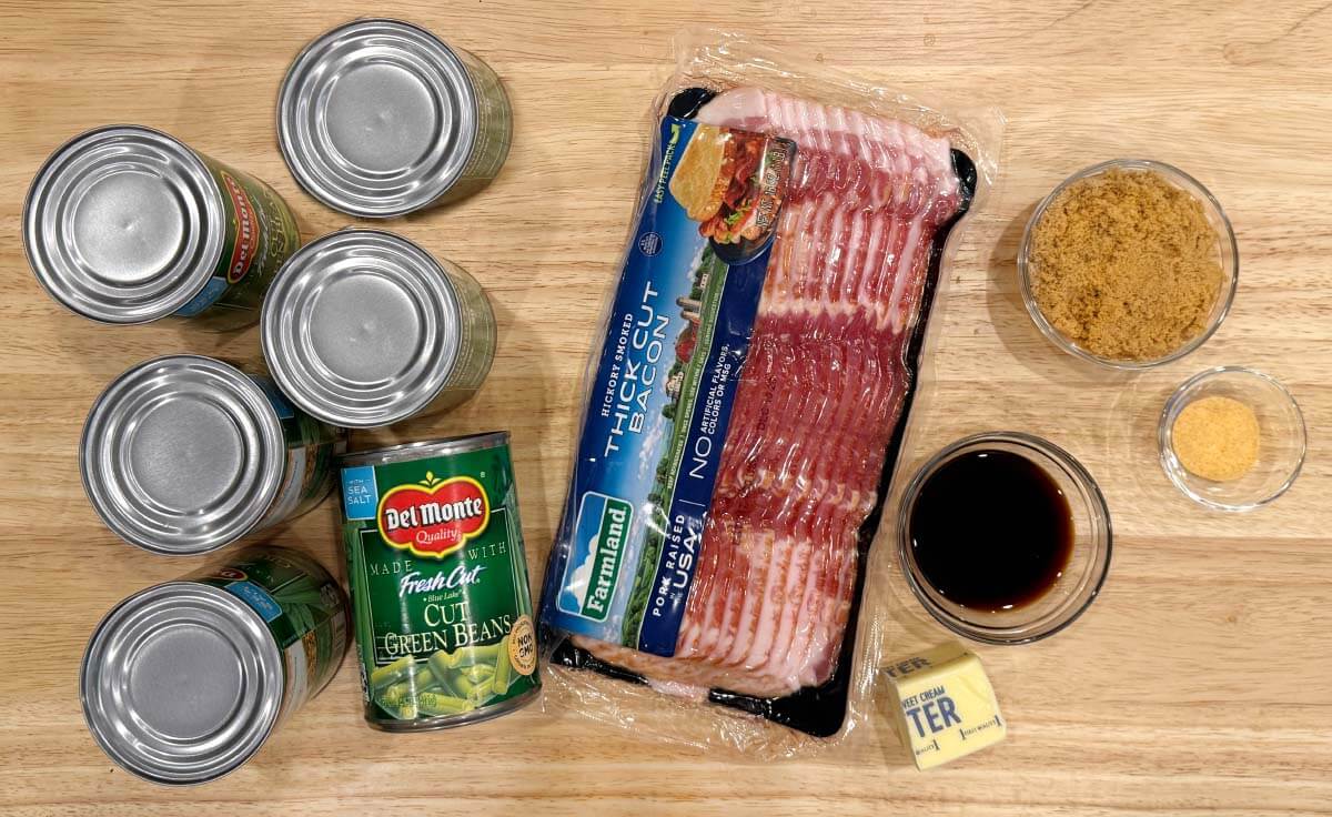 Canned green beans, bacon, brown sugar, butter, low-sodium soy sauce, and garlic powder arranged on a wooden surface