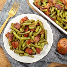 Brown sugar bacon green beans served on a white plate with a gold fork beside the casserole dish