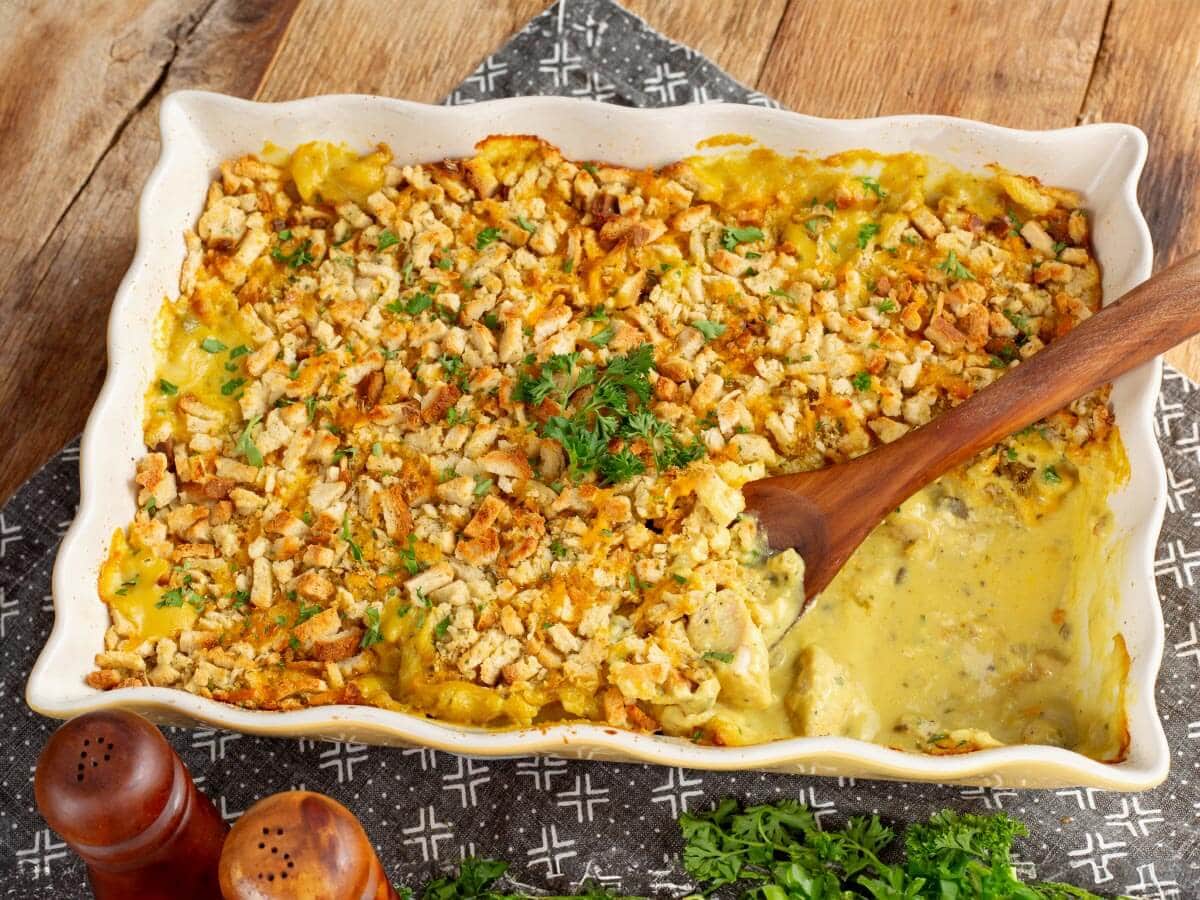 Chicken and stuffing casserole in a white baking dish with golden stuffing and a wooden serving spoon