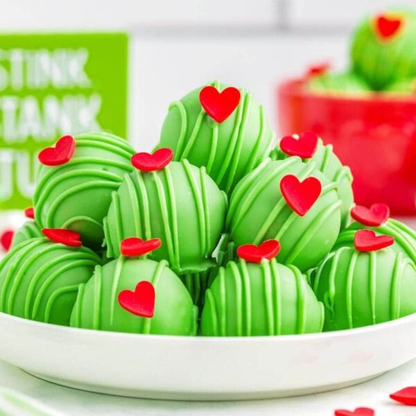 Grinch Truffles with green candy drizzle and red heart sprinkles piled on a white plate