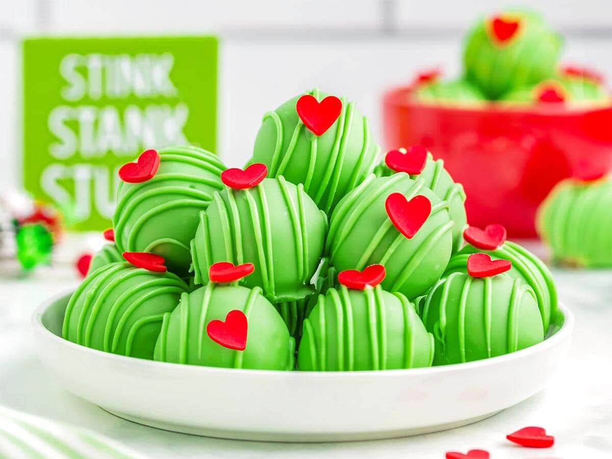 Grinch Truffles with green candy drizzle and red heart sprinkles piled on a white plate