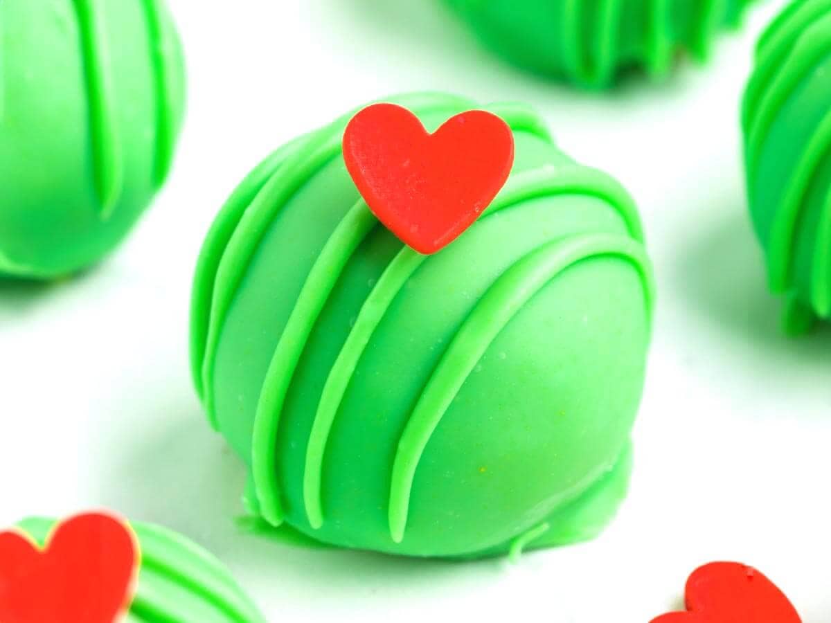 Close-up of a Grinch Truffle with a smooth green candy coating, green drizzle, and a red heart