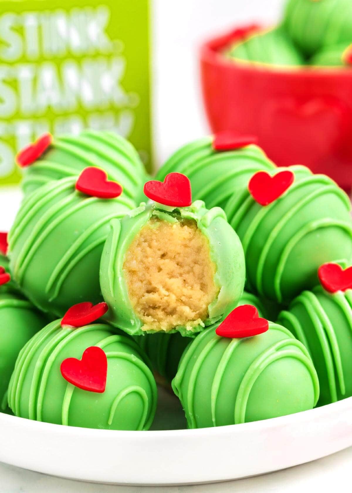 Grinch Truffles on a white plate, with one bitten open to show the creamy golden cookie filling