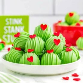 Grinch Truffles piled on a white plate, decorated with green drizzle and red heart sprinkles