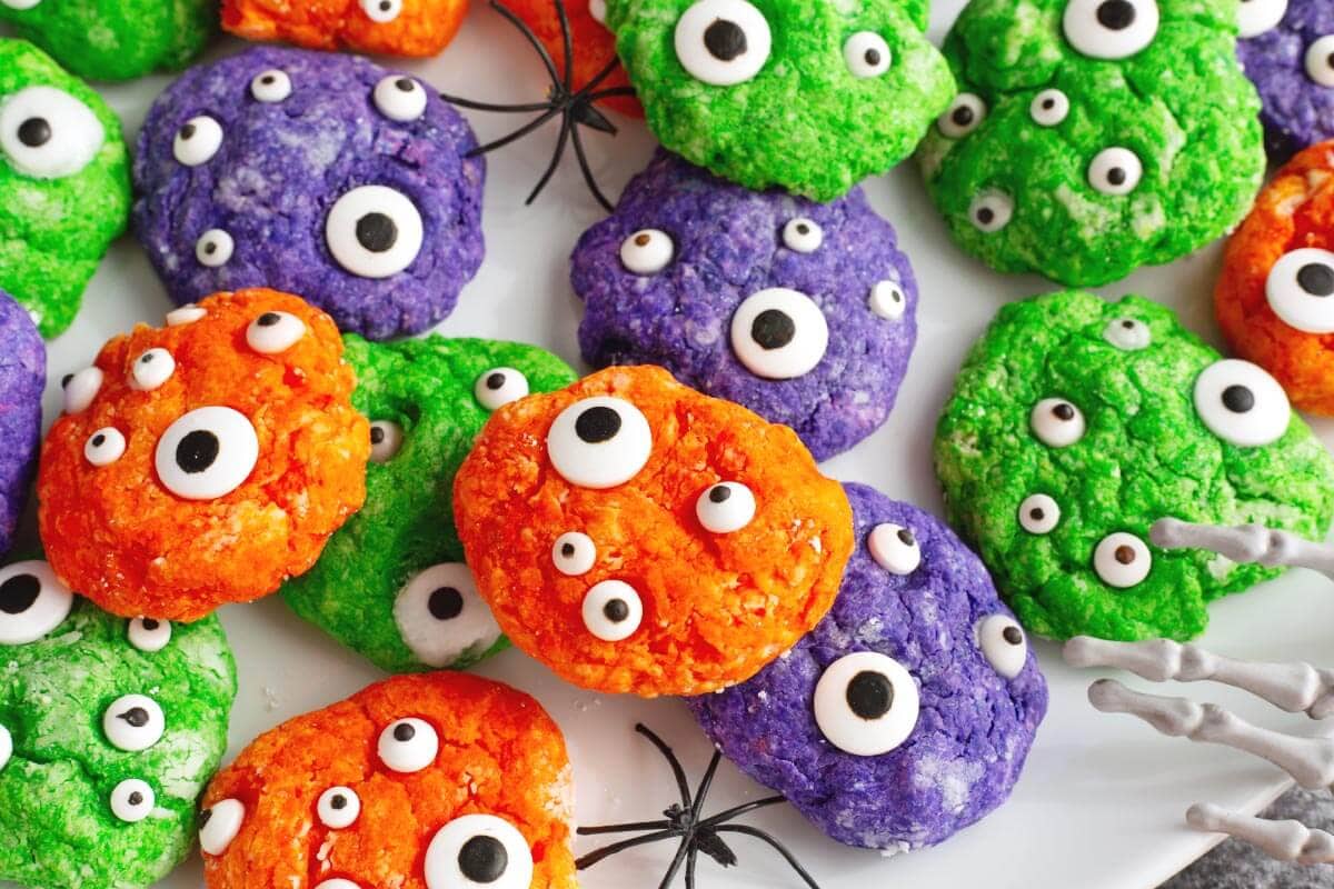 Close-up of colorful Halloween Monster Cookies decorated with assorted candy eyes on a white platter.