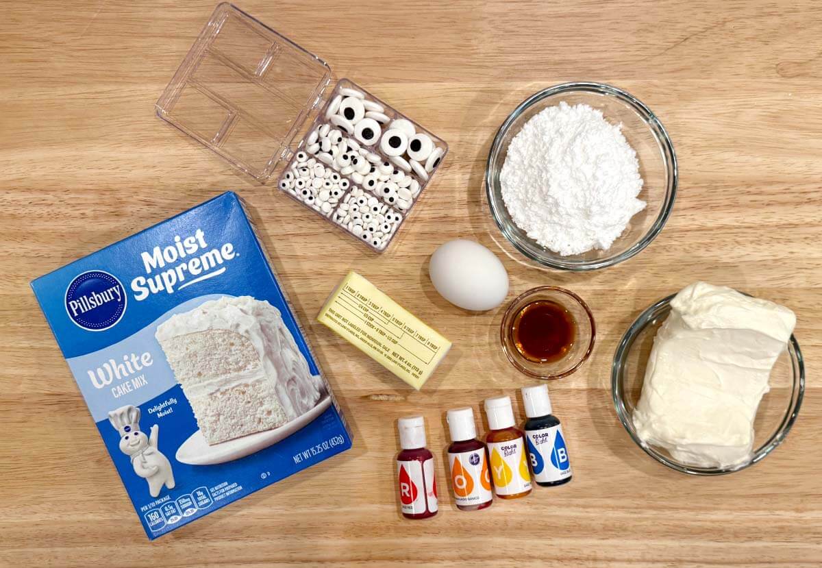 Ingredients for Halloween Monster Cookies, including white cake mix, cream cheese, butter, egg, vanilla, powdered sugar, food coloring, and candy eyes.