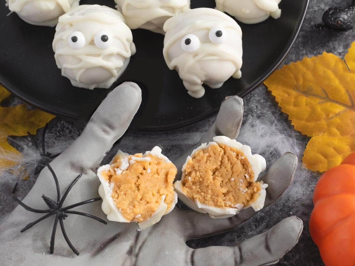 Halved white chocolate Oreo truffle showing the golden cookie filling on a gray Halloween hand