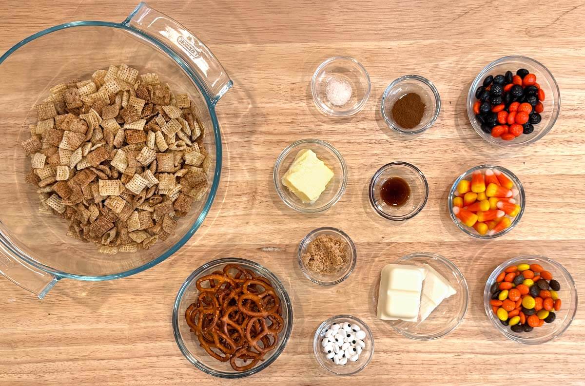Ingredients for Halloween Snack Mix, including Cinnamon Chex, pretzels, butter, white melting chocolate, and assorted Halloween candies.