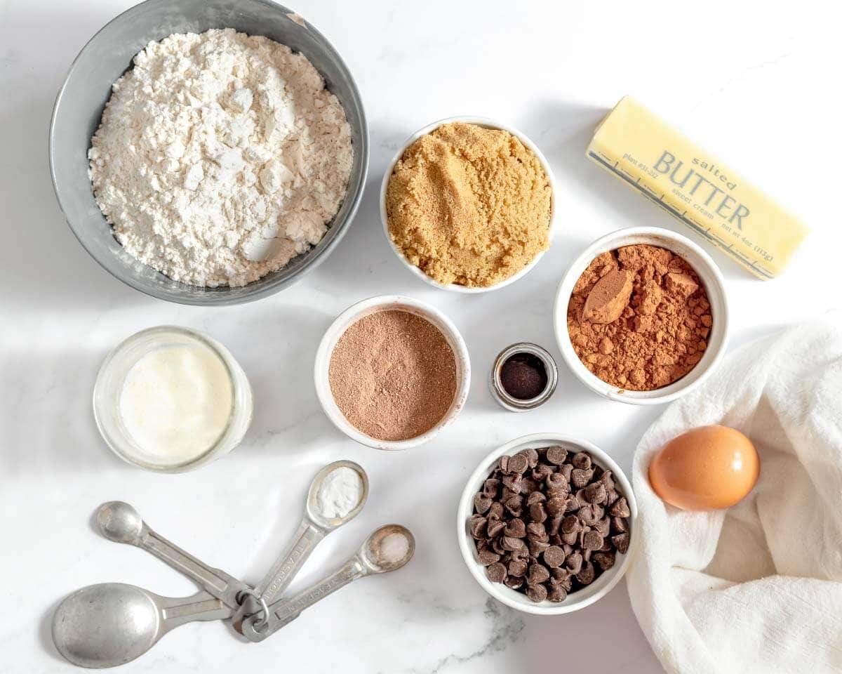 Ingredients for hot cocoa cookies, including flour, cocoa powder, hot cocoa mix, butter, brown sugar, egg, cream, and chocolate chips