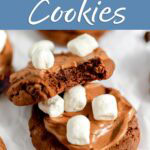 Hot cocoa cookies with chocolate frosting and mini marshmallows, with a bite taken out of one to show the chocolate center