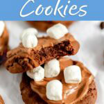 Hot cocoa cookies with chocolate frosting and mini marshmallows, with a bite taken out of one to show the chocolate center