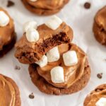 Close-up of a bitten hot cocoa cookie stacked on a frosted cookie, both topped with mini marshmallows