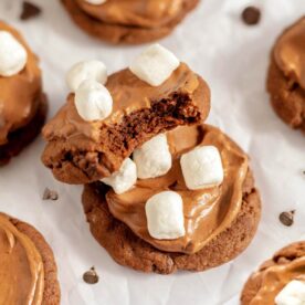 Close-up of a bitten hot cocoa cookie stacked on a frosted cookie, both topped with mini marshmallows