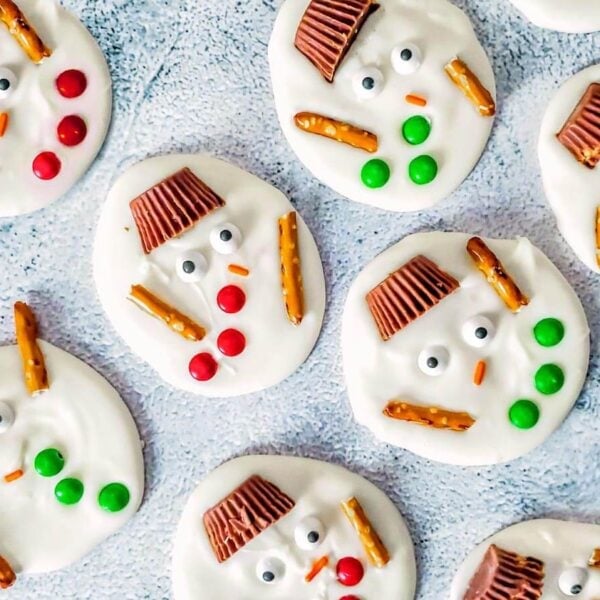 Melted snowman bark with peanut butter cup hats, candy eyes, red and green buttons, and pretzel arms.