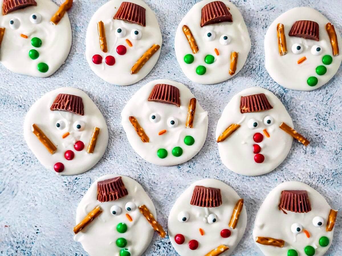 Melted snowman bark with peanut butter cup hats, candy eyes, red and green buttons, and pretzel arms.