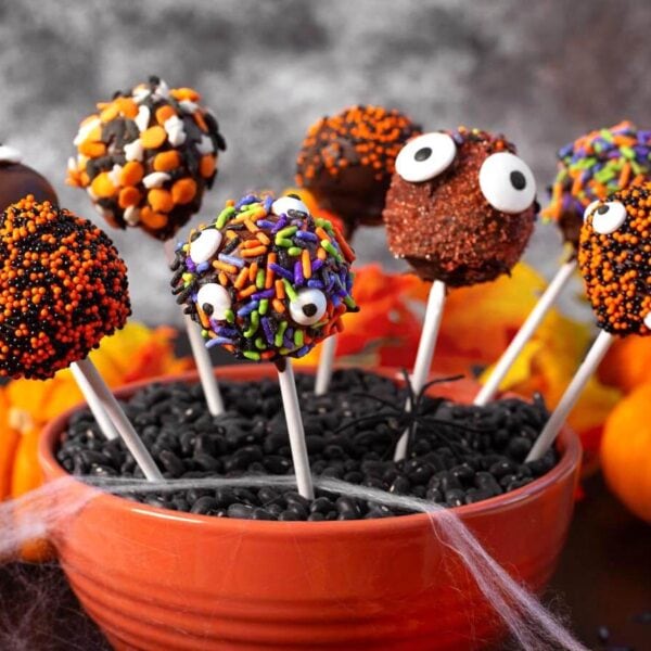Halloween cake pops dipped in chocolate and decorated with colorful sprinkles and candy eyes in an orange bowl