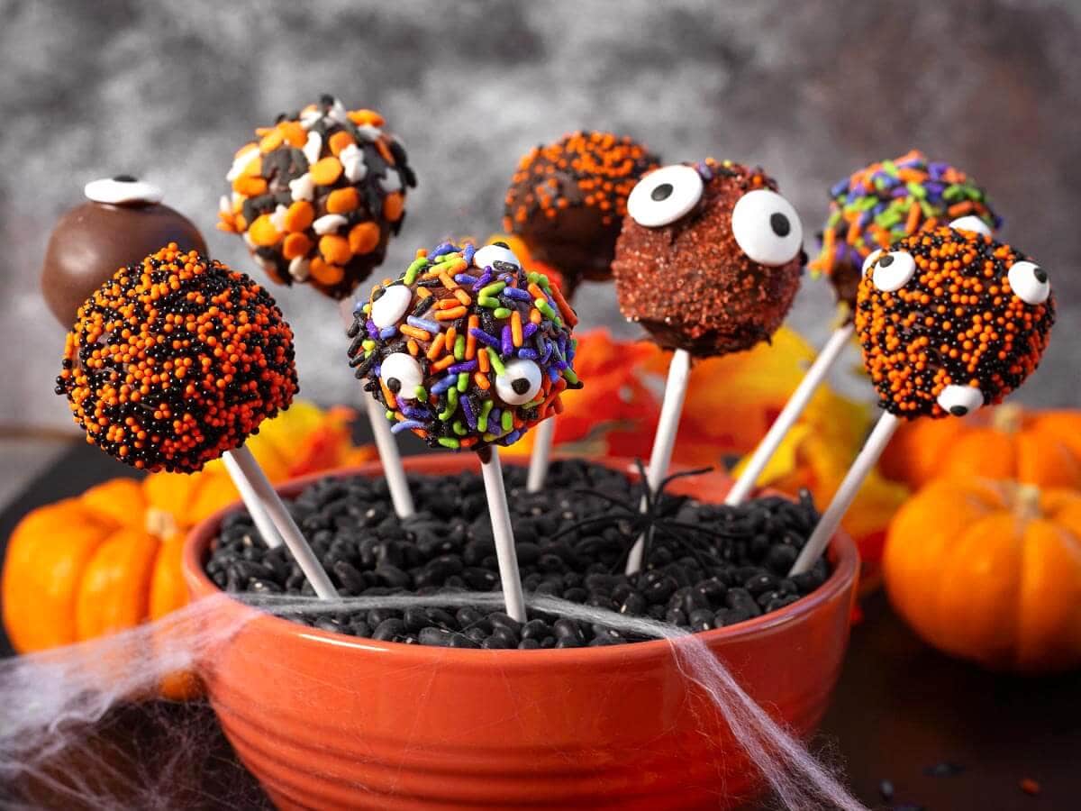 Halloween cake pops dipped in chocolate and decorated with colorful sprinkles and candy eyes in an orange bowl