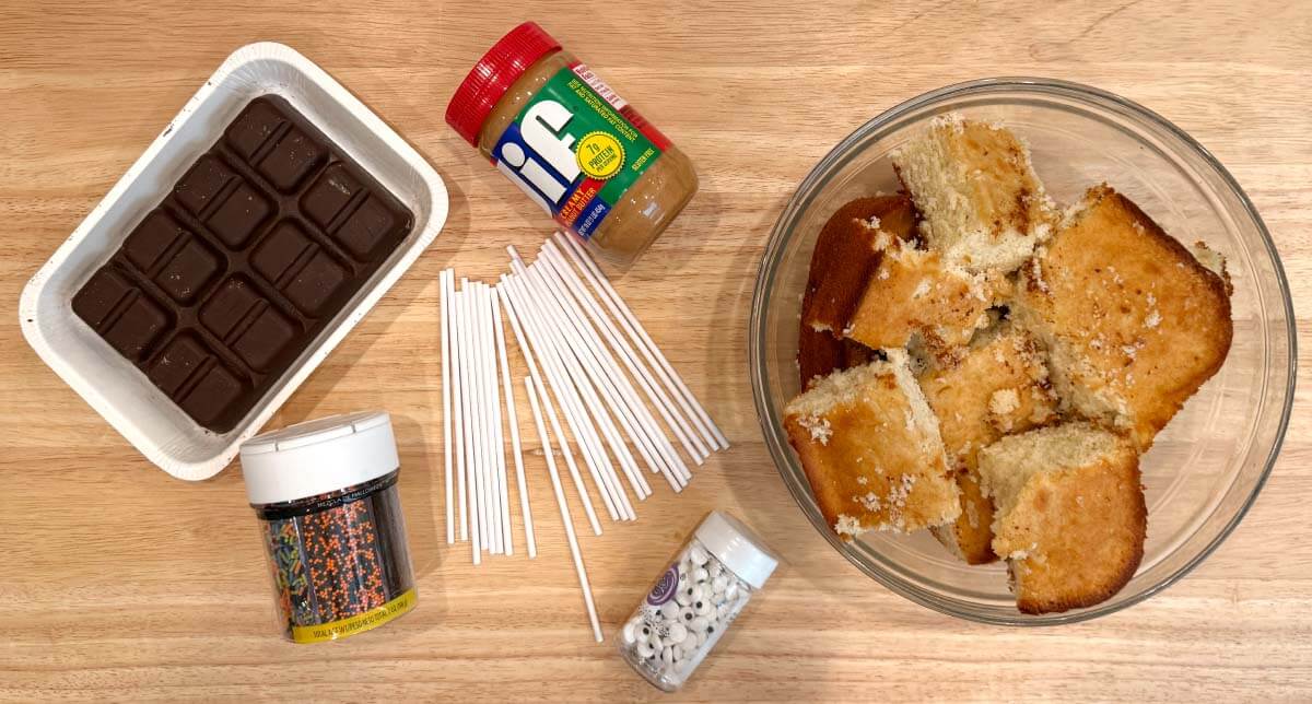 Ingredients for Halloween cake pops including crumbled cake, creamy peanut butter, melting chocolate, sprinkles, and candy eyes