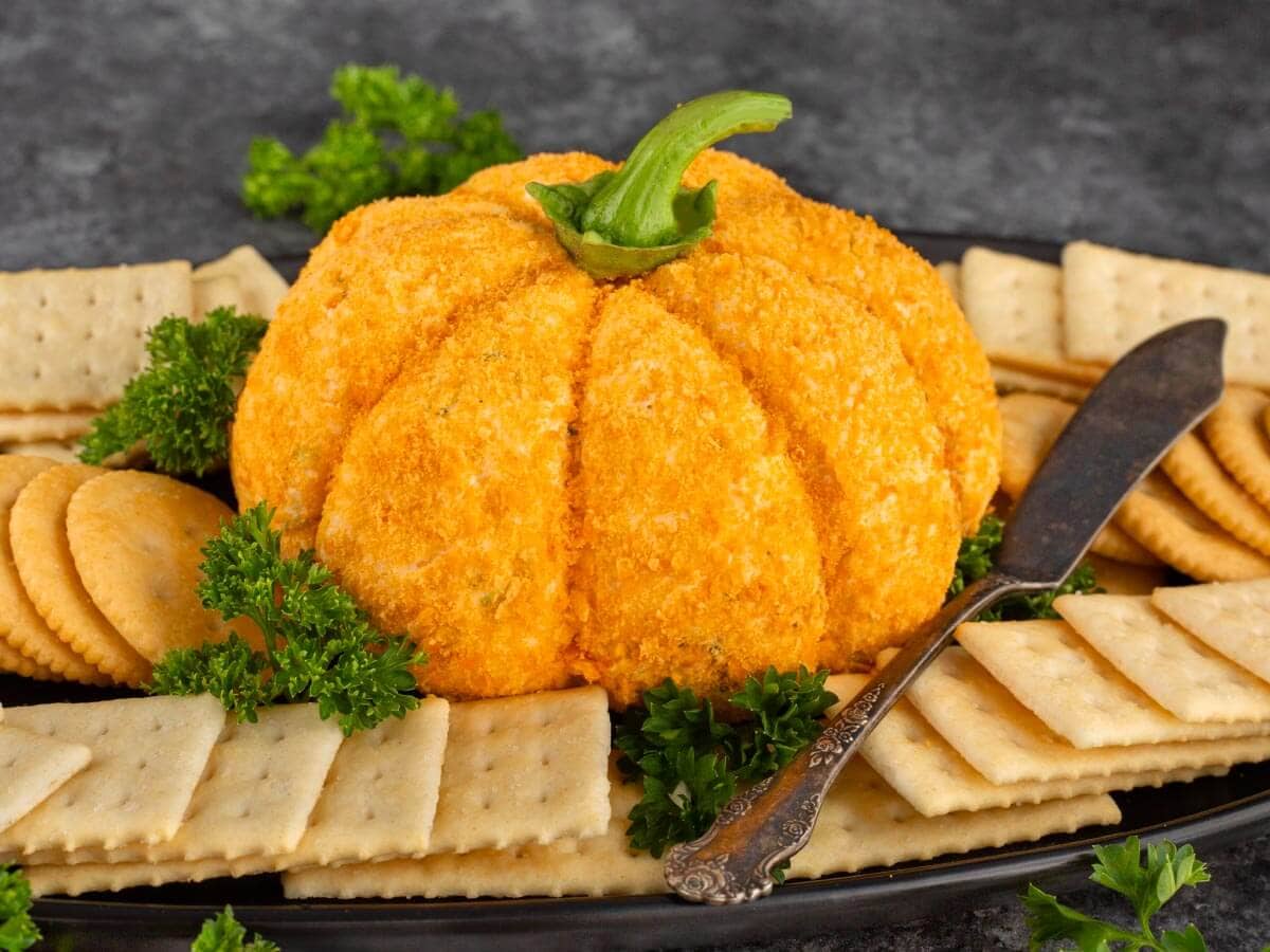 Pumpkin cheese ball and crackers on a black platter