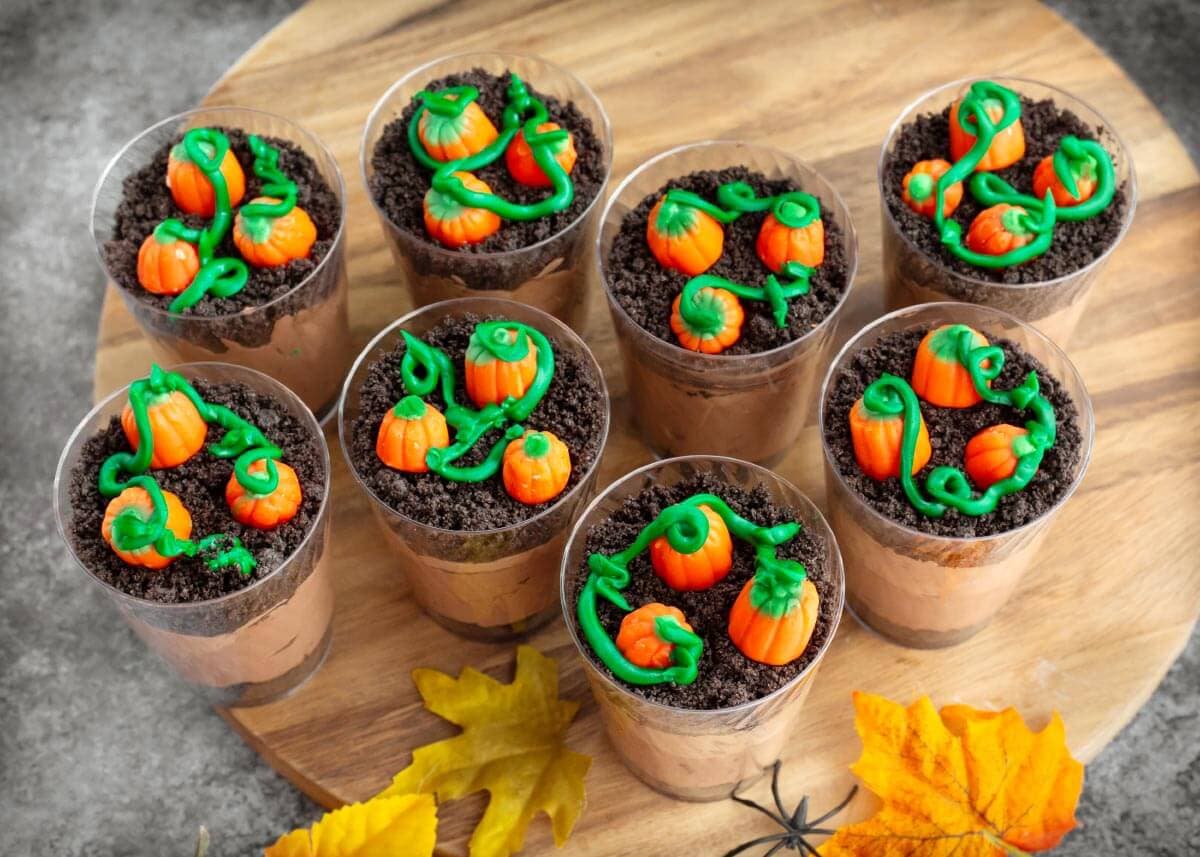 Overhead view of eight Pumpkin Patch Dirt Cups decorated with candy pumpkins and green frosting vines