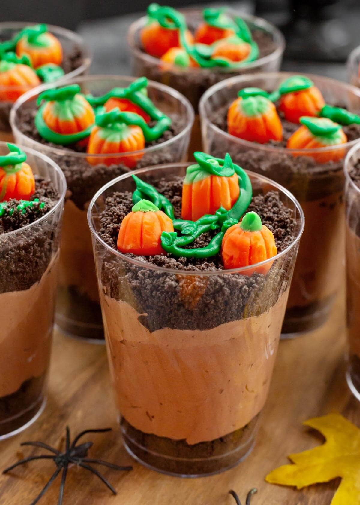 Close-up of a pumpkin patch pudding cup with crushed Oreo dirt, orange candy pumpkins, and green icing vines