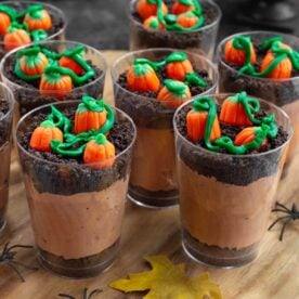 Two Halloween dirt cups with layers of chocolate pudding, Oreo crumbs, candy pumpkins, and green icing vines